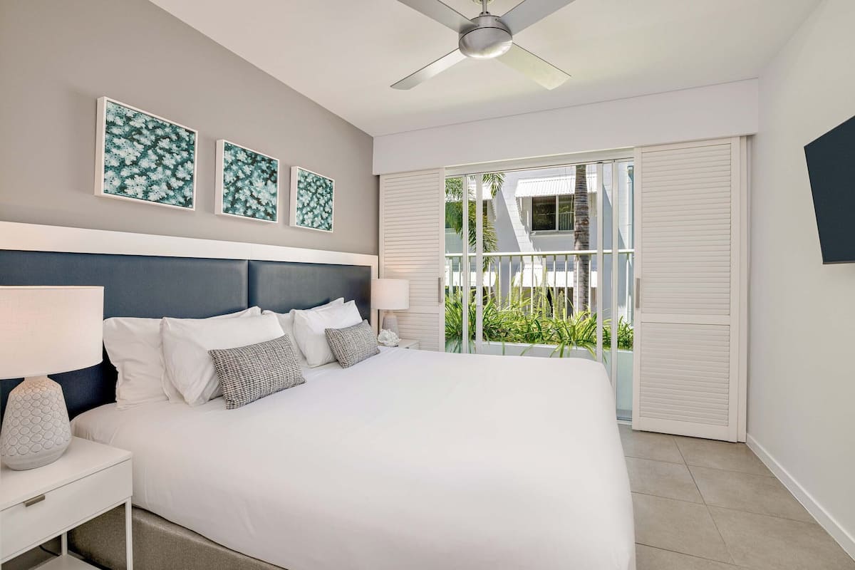 A modern bedroom with a large bed, a ceiling fan, and a view of the outdoors through a sliding door.
