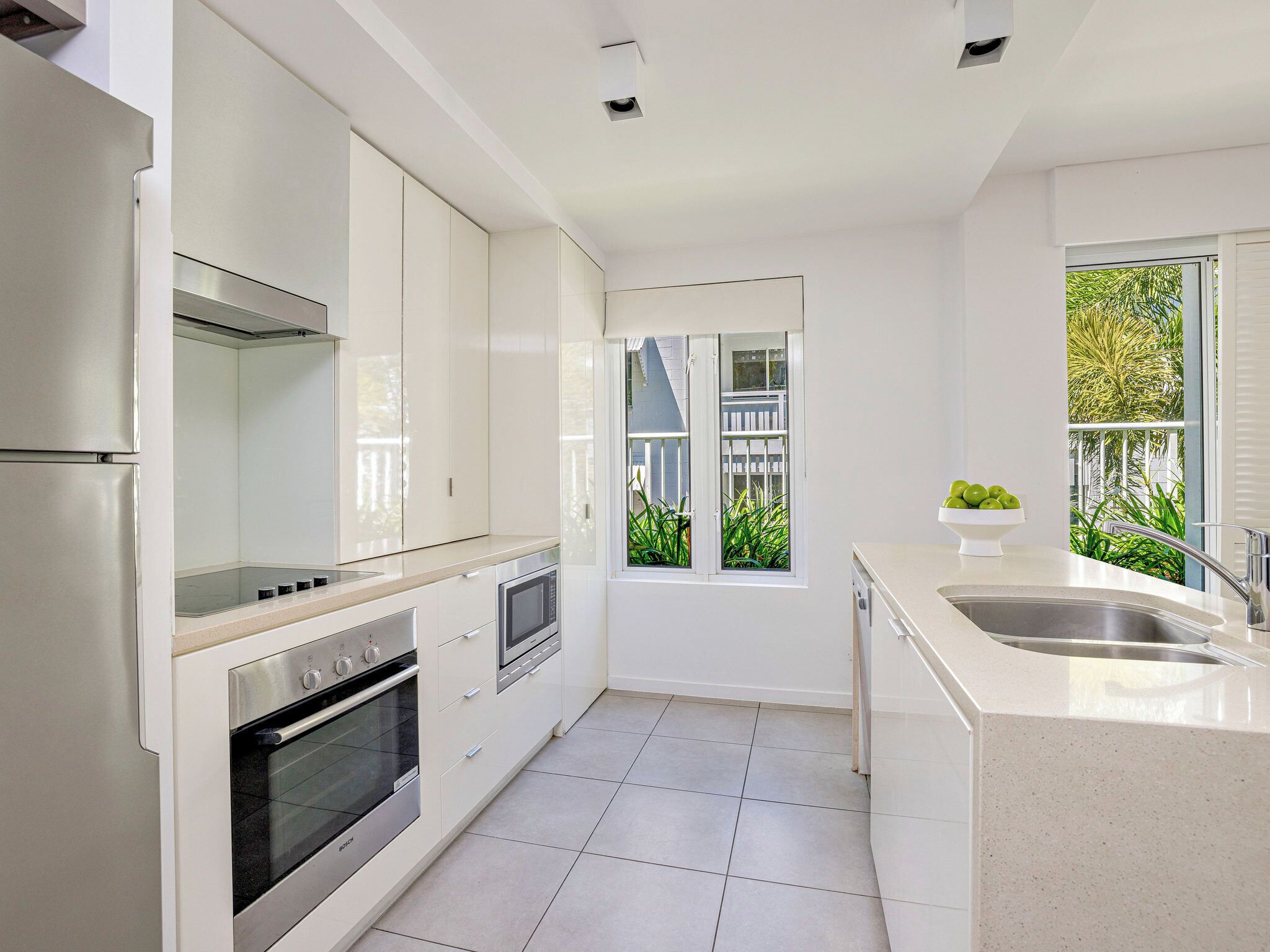 Een moderne keuken met witte kasten, roestvrijstalen apparatuur en een groot raam met uitzicht.