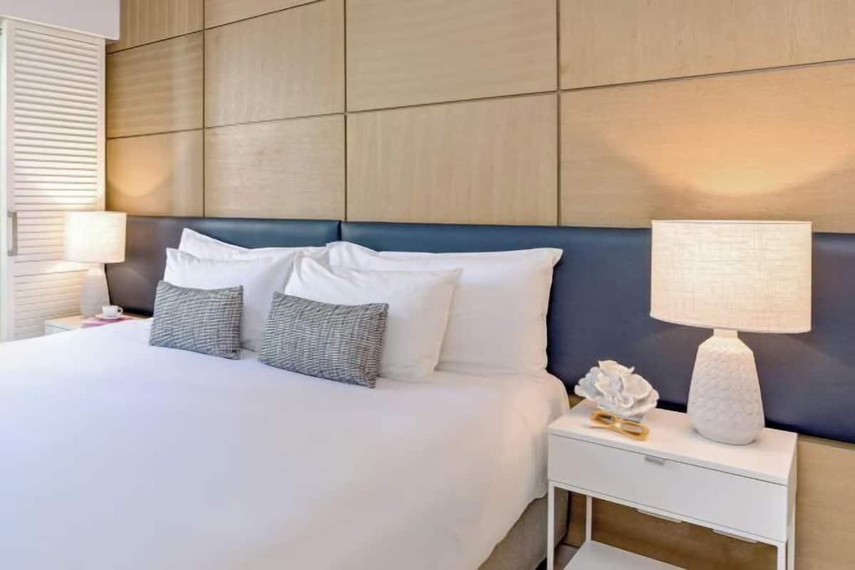 A hotel room with a large bed, a nightstand with a lamp, and a wall panel design.