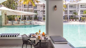 A poolside dining area with a table set for two, overlooking a pool and a resort building. - Peppers Beach Club (Port Douglas)