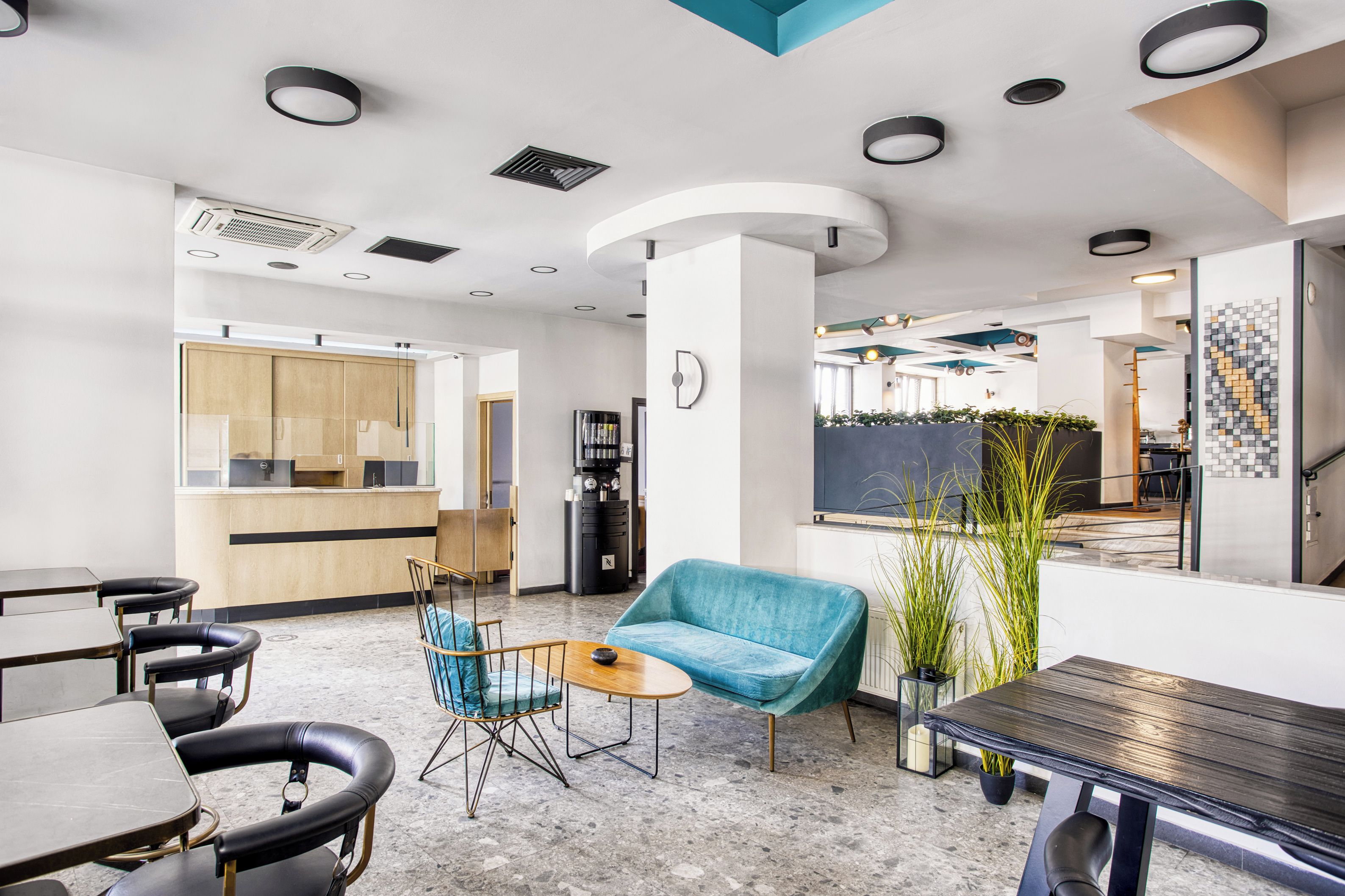Un interior moderno con mostrador de recepción, zona de estar con sofá y sillones, una cafetera y un ventanal grande.