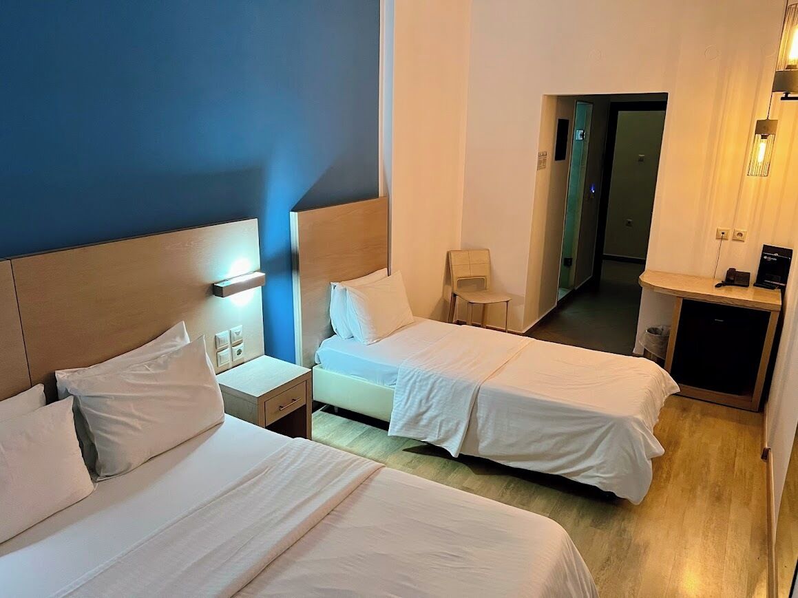 Een hotelkamer met twee bedden, een bureau, een stoel en een kleine kitchenette.