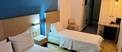 Een hotelkamer met twee bedden, een bureau, een stoel en een kleine kitchenette.