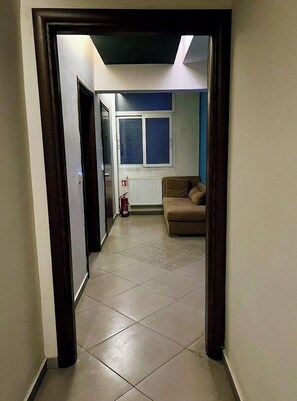 A hallway leading to a living area with a brown sofa, a window, and a radiator. - Hotel Rotonda (Thessaloniki)