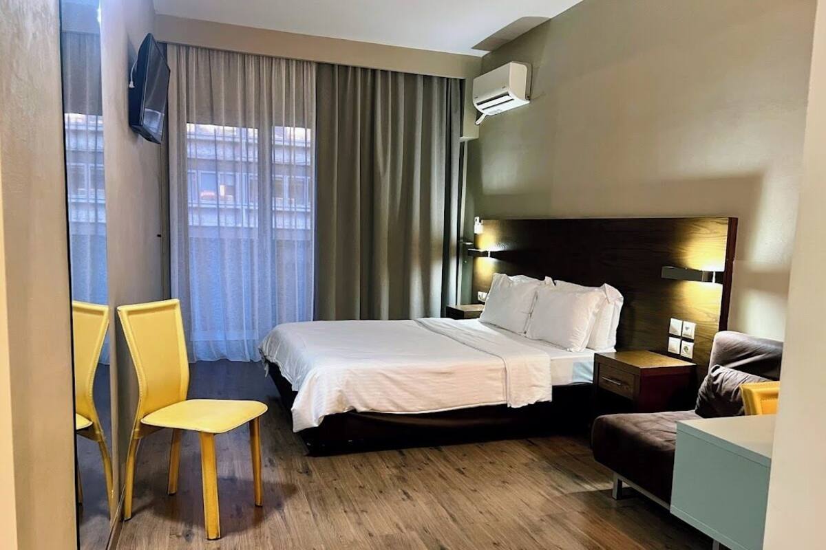 A hotel room with a bed, a desk, a chair, and a TV mounted on the wall.