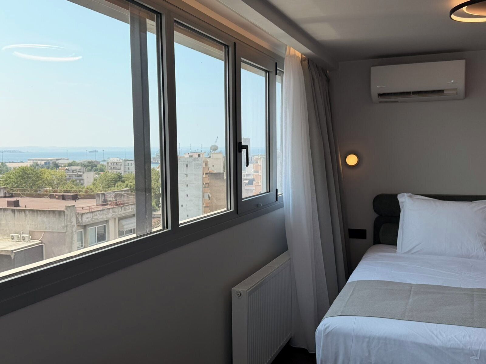 Una habitación de hotel con un ventanal grande, una cama, un radiador y un equipo de aire acondicionado.