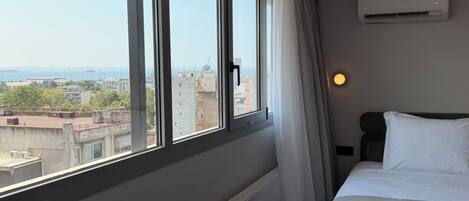 Una habitación de hotel con un ventanal grande, una cama, un radiador y un equipo de aire acondicionado.