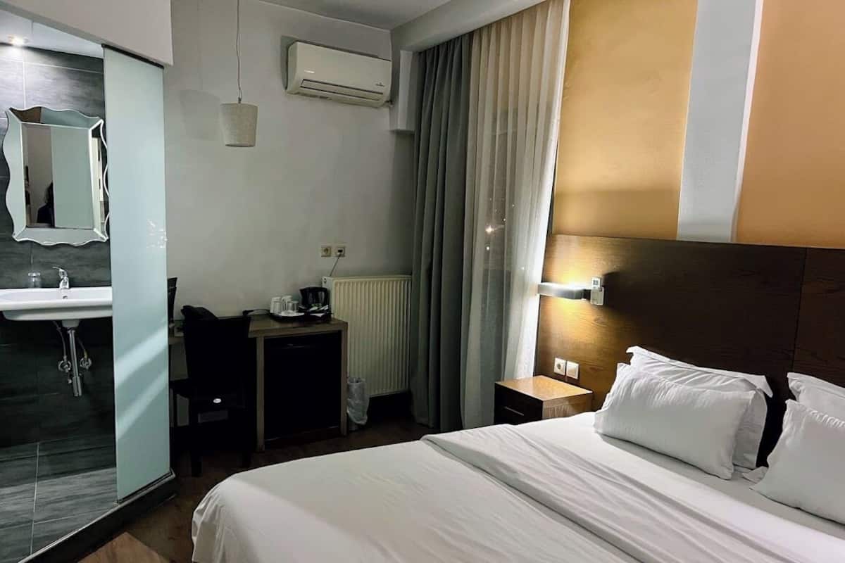 Ein Hotelzimmer mit Bett, Schreibtisch, Stuhl, Spiegel, Waschbecken und einem Fenster mit Vorhängen.