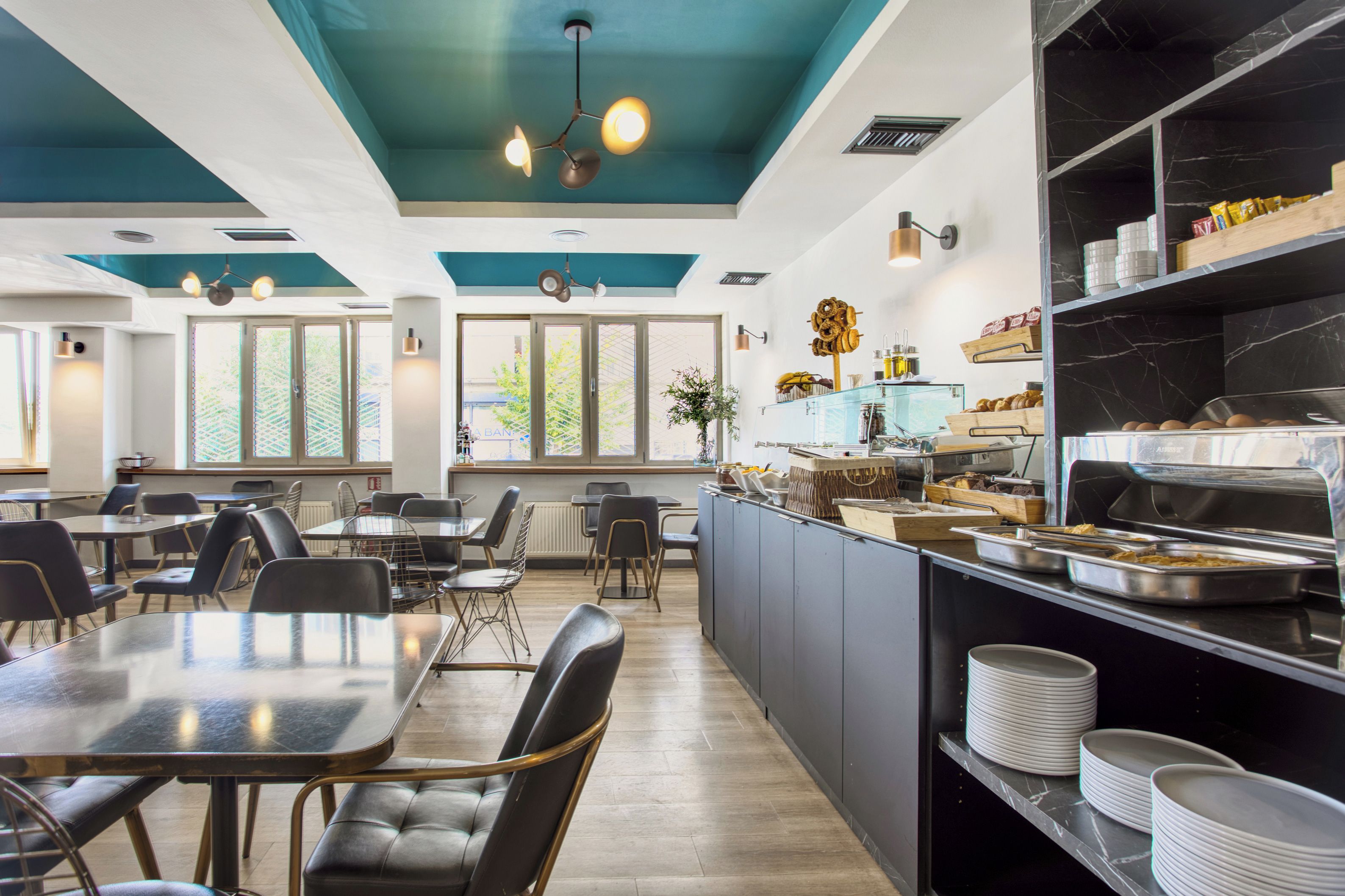 Ein modernes Restaurant mit einer zentralen Servierinsel, mehreren Sitzbereichen und einer türkisblauen Decke.