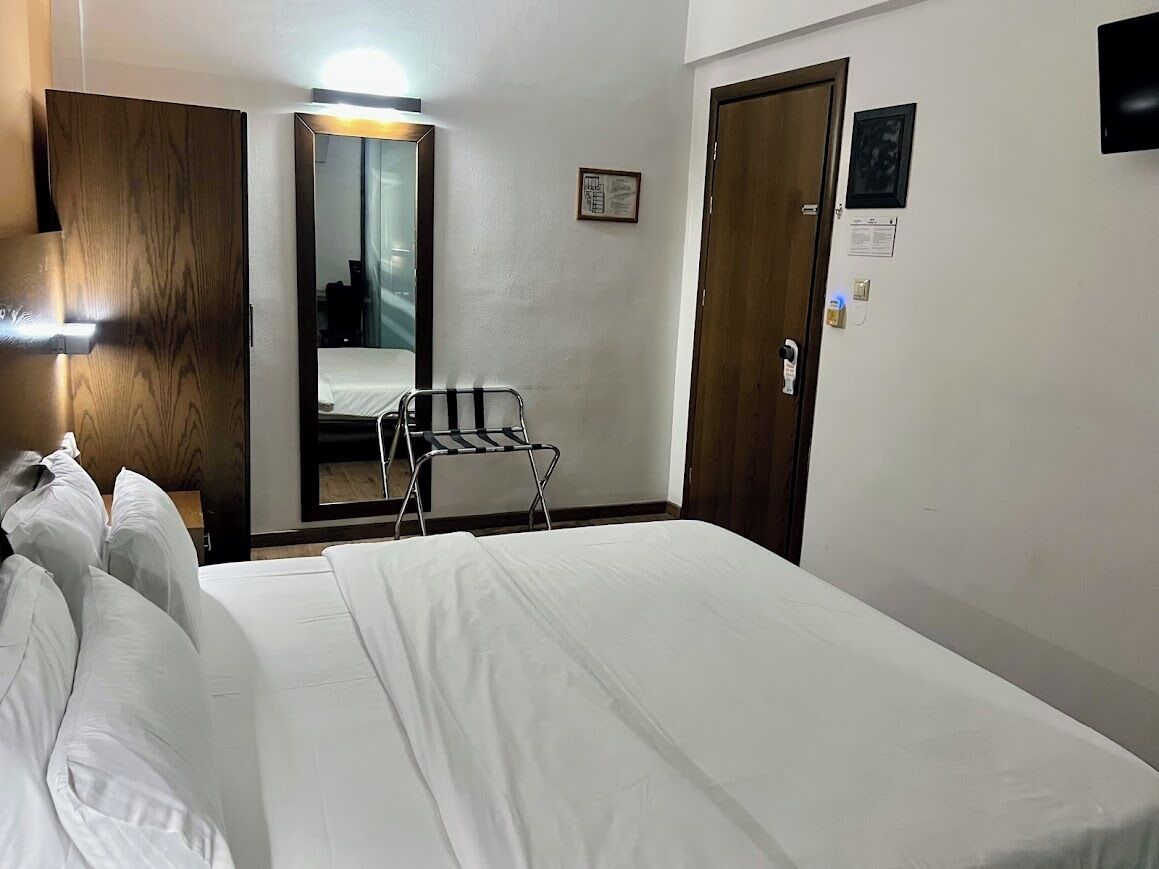 A hotel room with a bed, a mirror, a chair, and a door.
