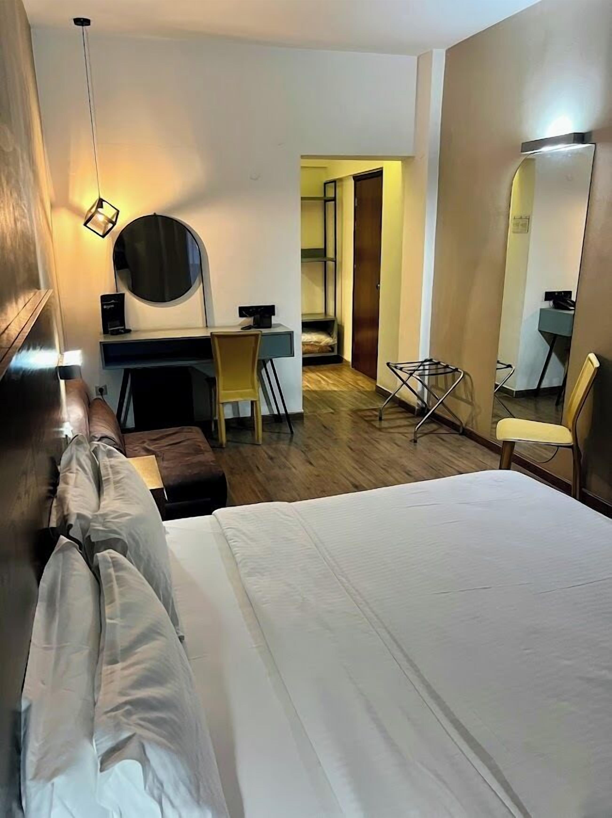 Ett hotellrum med en säng, ett skrivbord, en stol, en spegel och en garderob.