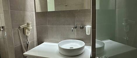 Un baño moderno con un espejo grande, un lavabo redondo y una zona de ducha.