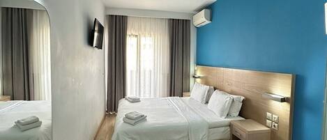 A hotel room with two beds, a TV, an air conditioner, a wooden headboard, and a small table.