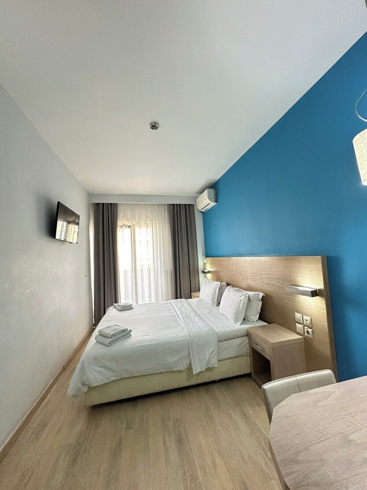 Ein Hotelzimmer mit Bett, Nachttisch, Ablagefläche und einem an der Wand befestigten Fernseher.