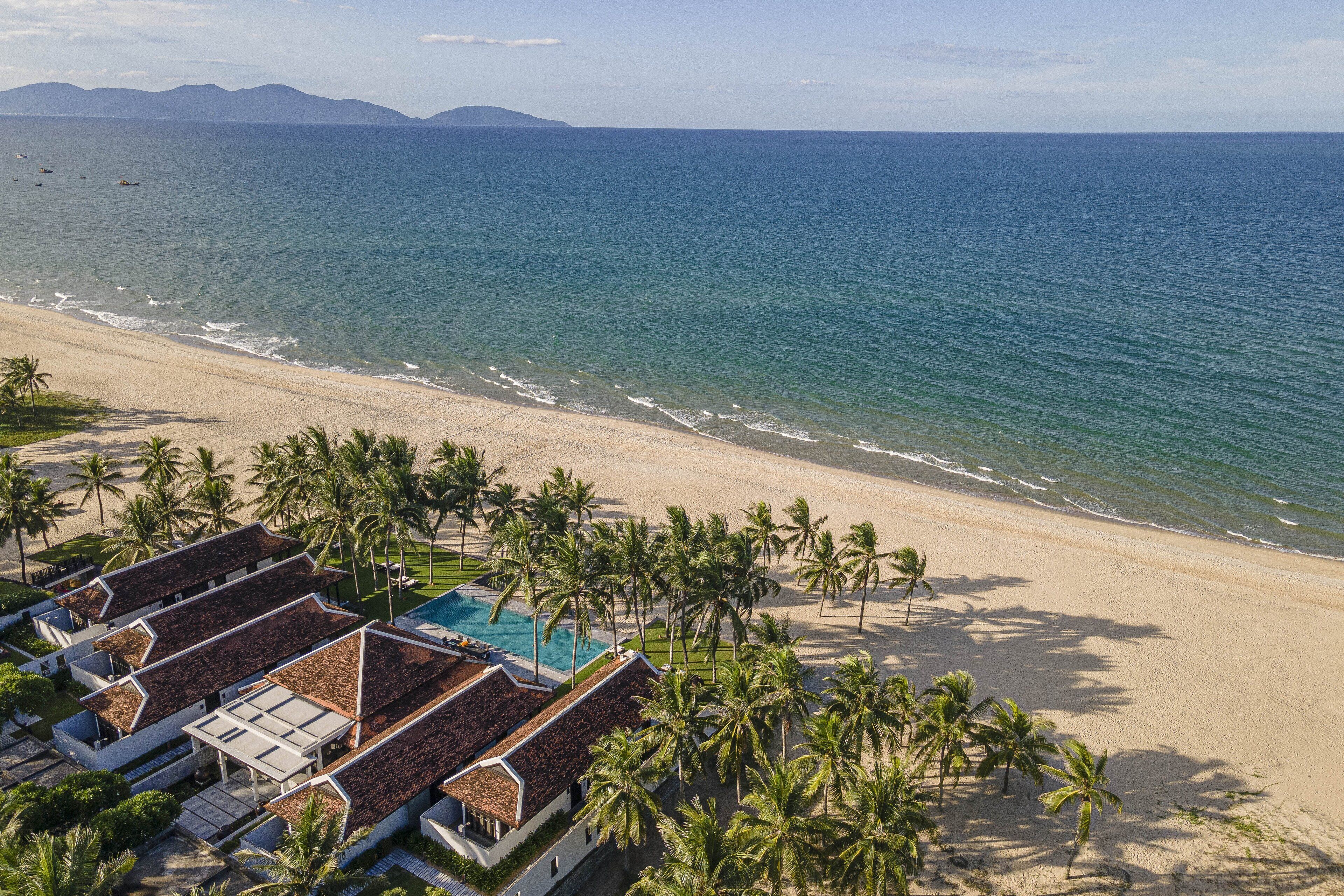 Un complejo turístico en la playa con varias villas, una piscina y palmeras.