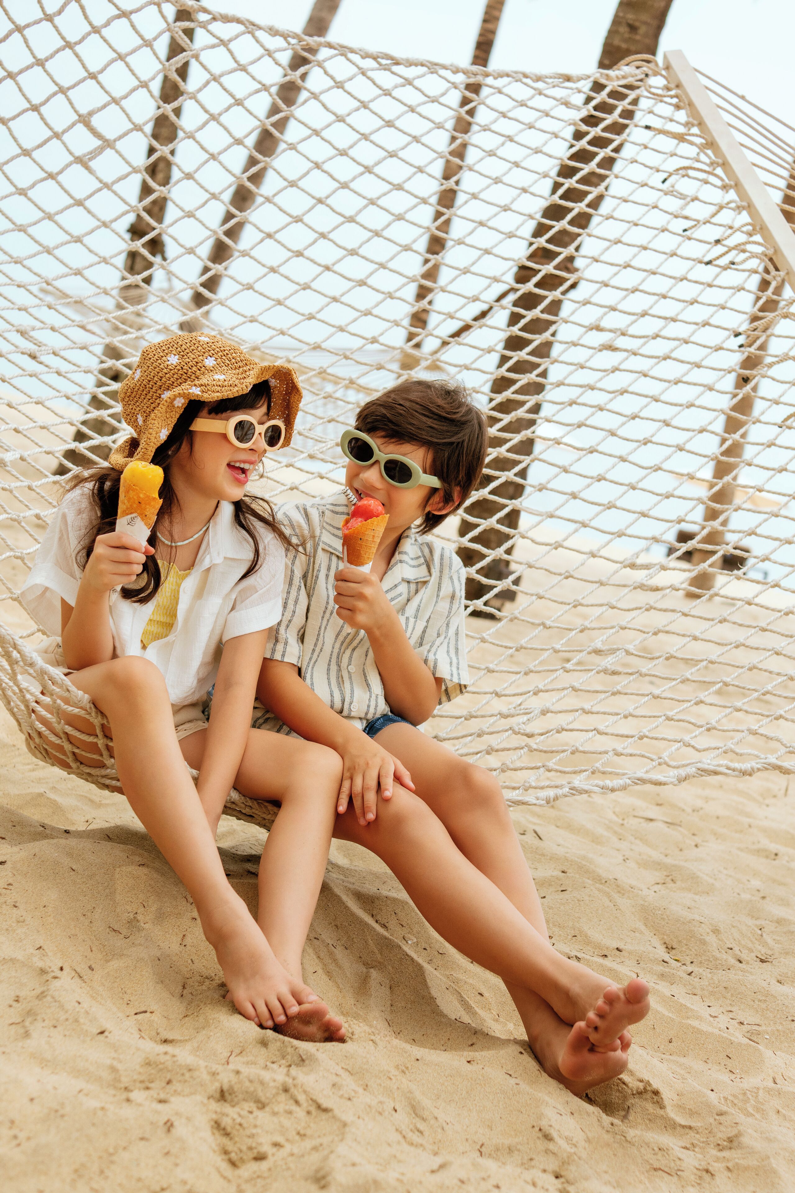 Two people sitting in a hammock on a sandy beach.