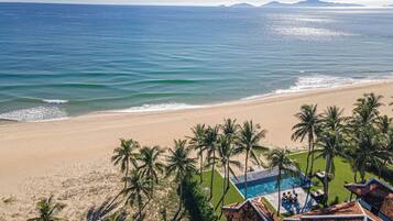 Vista de una playa con zona de piscina, palmeras y cielo despejado.