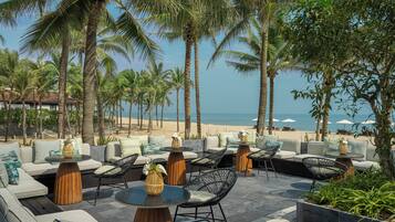 A beachside lounge with outdoor seating, palm trees, and a view of the ocean.