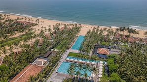 Luchtbeeld van een resort met een groot zwembad, strand en palmbomen.