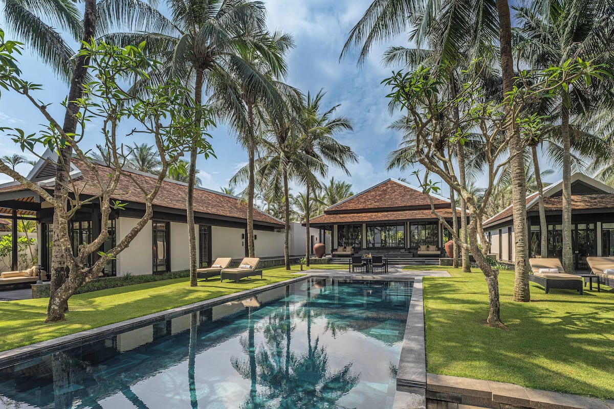 A poolside area with a clear pool, palm trees, and lounge chairs.
