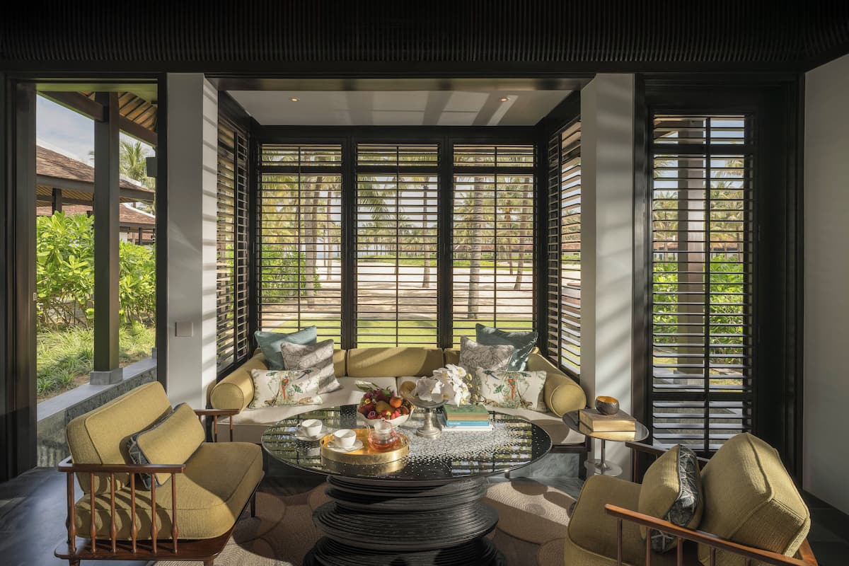 A modern living room with a glass coffee table, comfortable seating, and large windows with blinds.