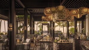 Een terras met rieten meubels, een stenen bargedeelte en hangende decoratieve verlichting.