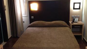 A hotel room with a bed, a nightstand with a phone, a wall-mounted light, and a door with curtains.