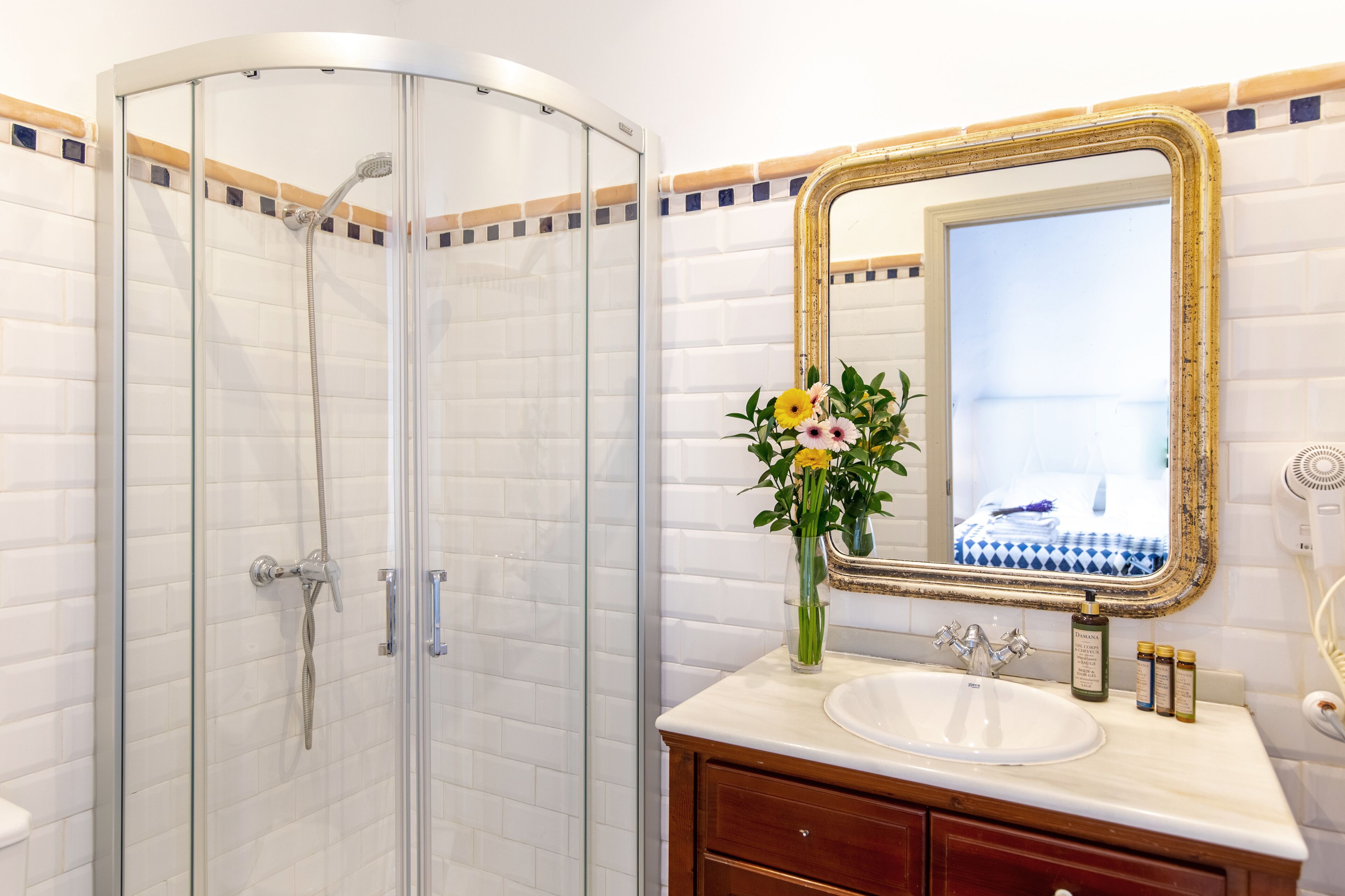 A bathroom with a glass-enclosed shower, a sink with a mirror, and a vase with flowers.