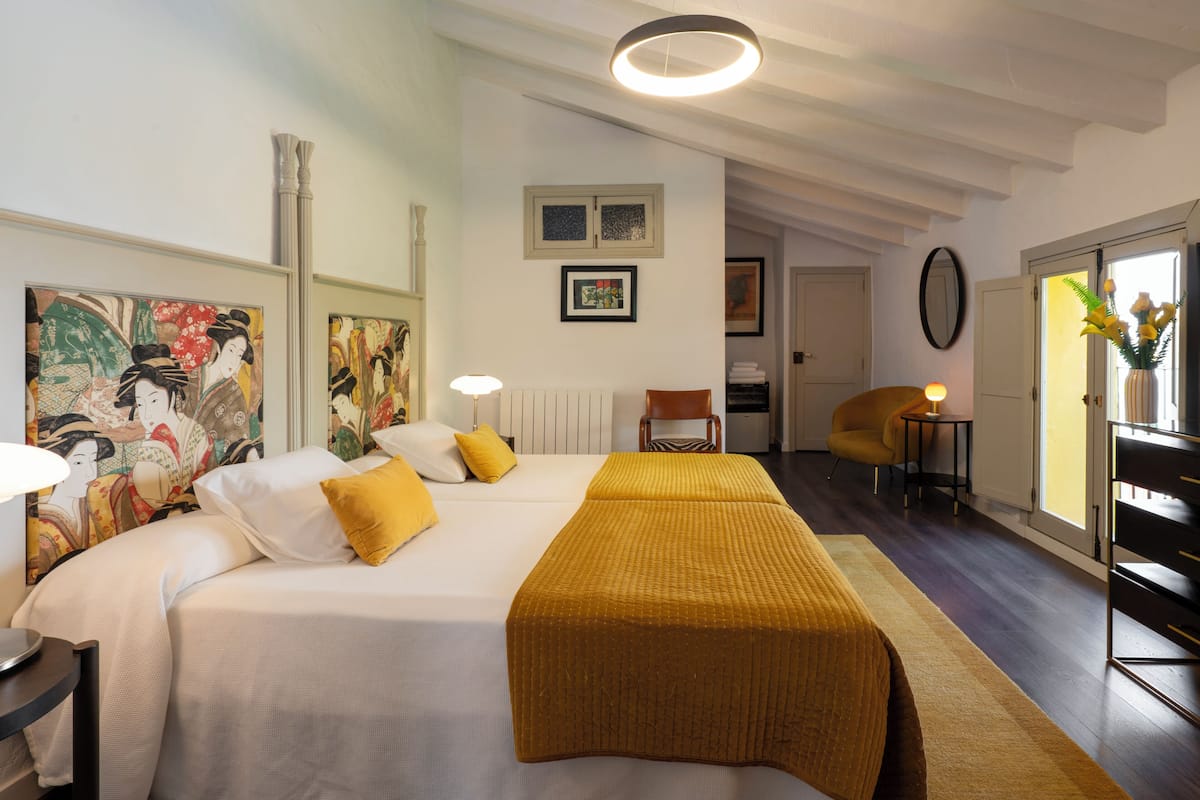 Habitació d'hotel amb un llit gran, una taula petita, una cadira i obres d'art a les parets.
