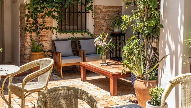 Eine Terrasse mit Korbmöbeln, einem Tisch mit Früchten und Gebäck sowie Topfpflanzen.