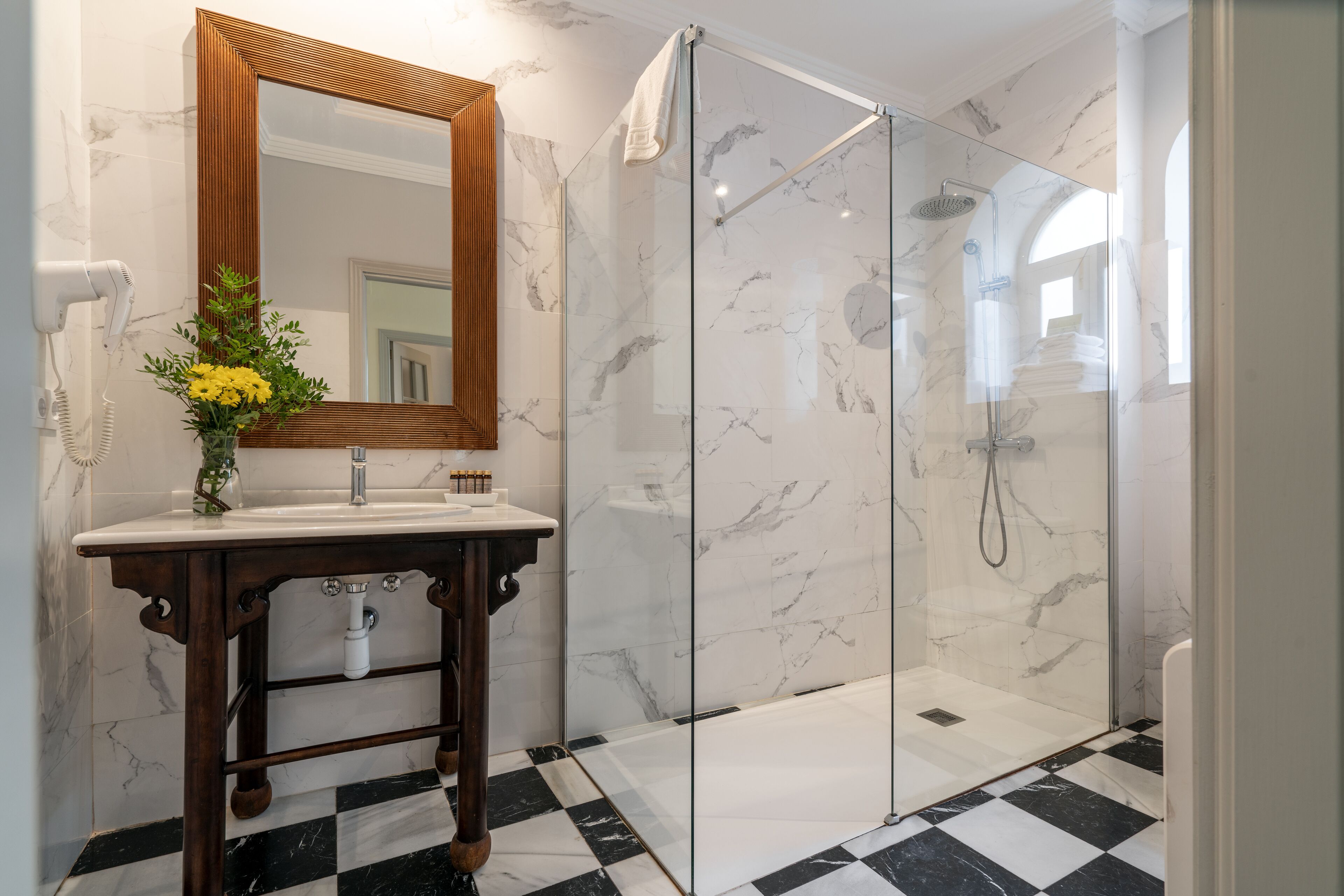 Un baño con ducha de mármol, tocador de madera y suelo a cuadros.