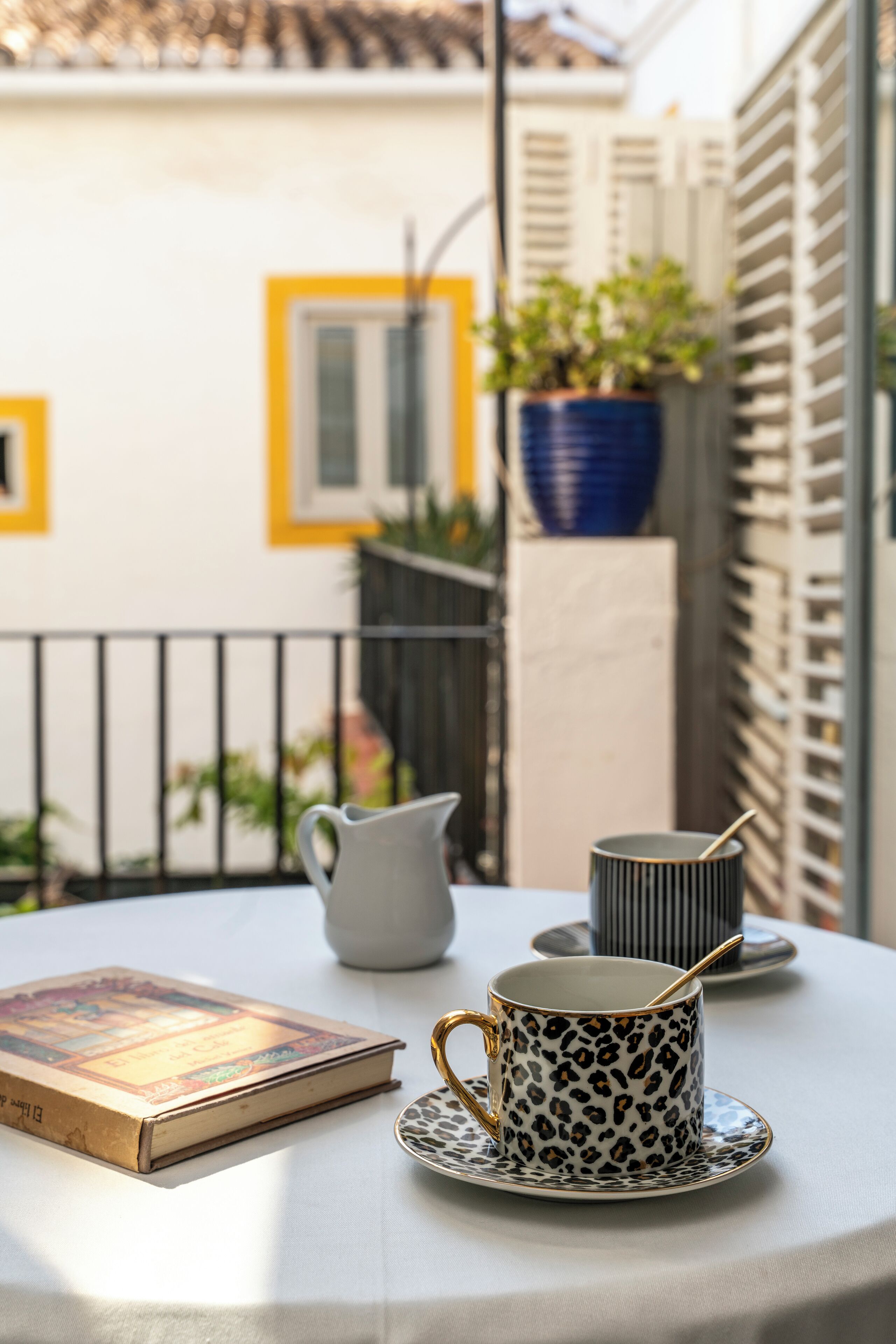 Ein Tisch mit einem Buch, einer Kanne und einer Tasse mit Löffel auf einer weißen Tischdecke.