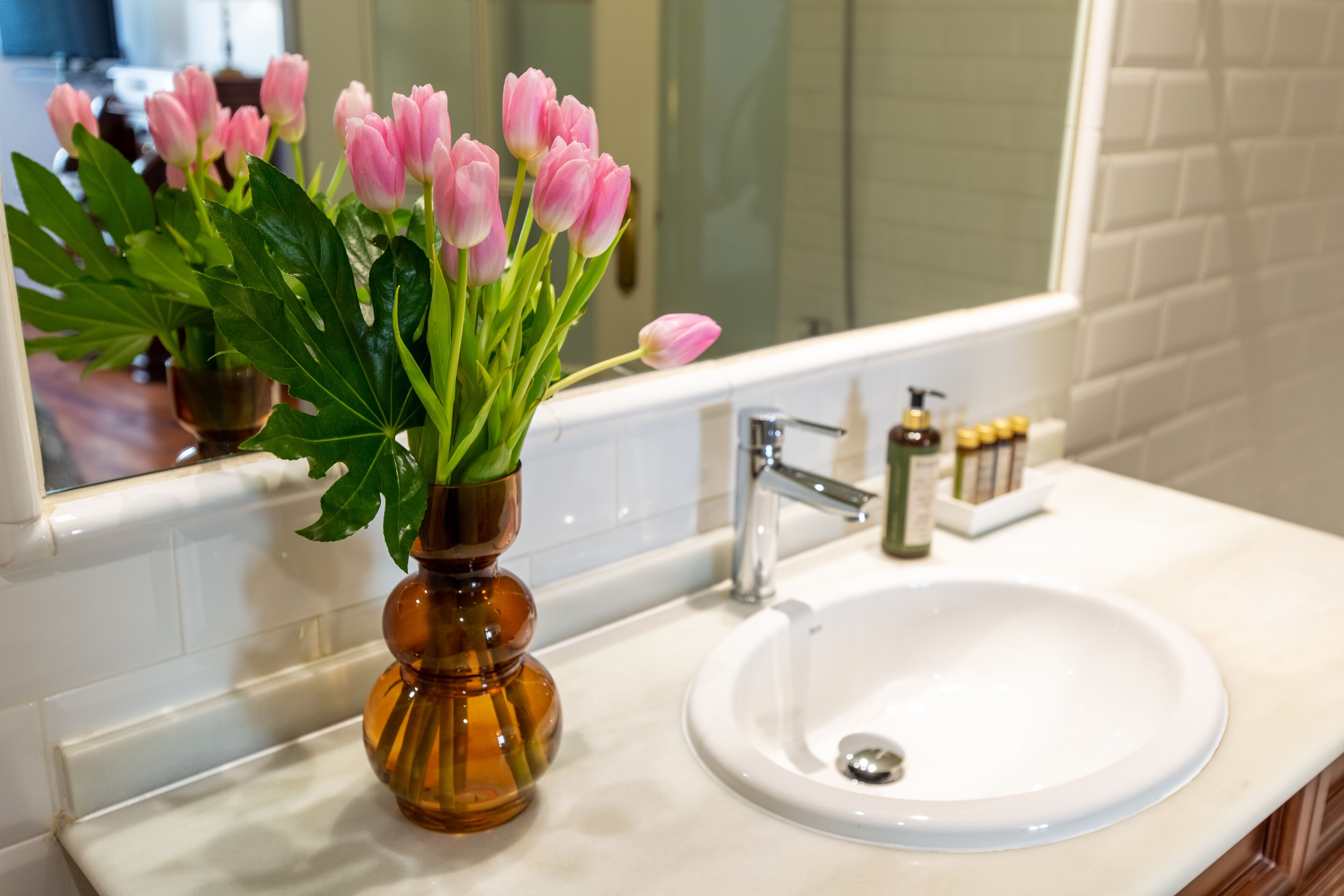 A bathroom with a white sink, a mirror, and a vase of pink tulips.