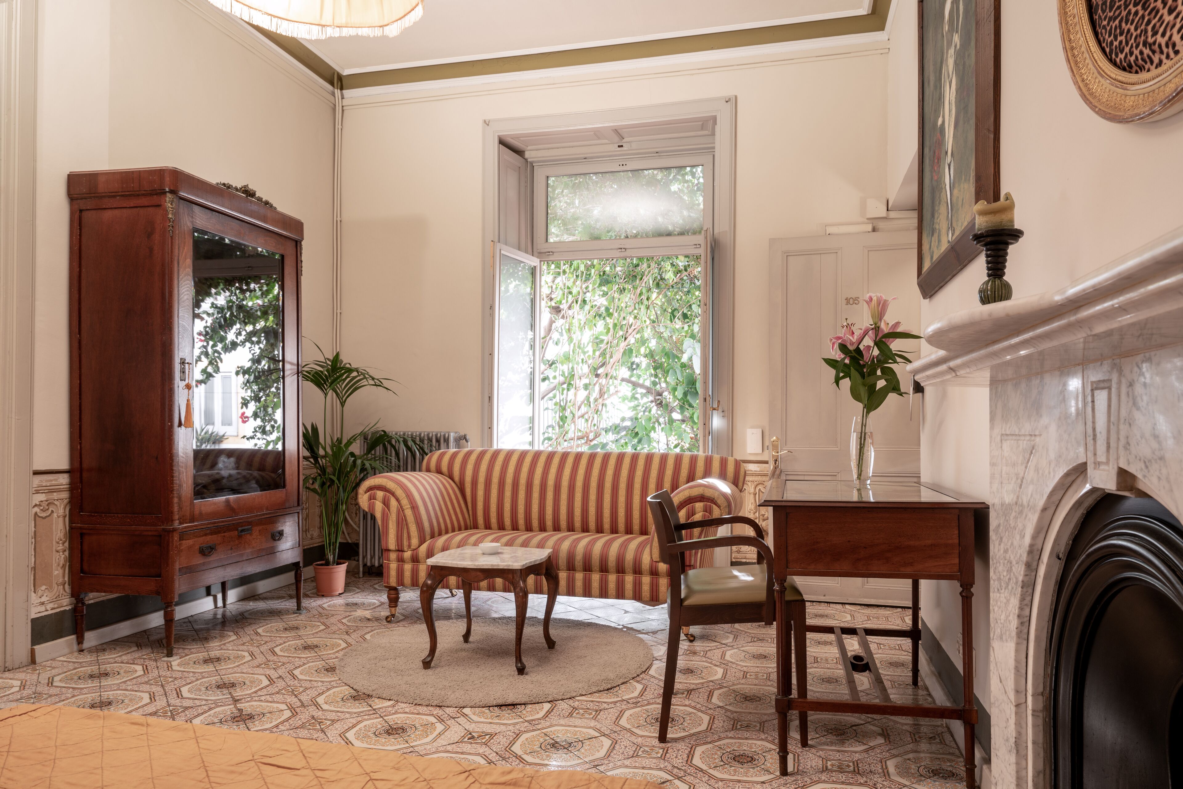 A living room with a sofa, a wooden cabinet, a fireplace, and a large window with a view of greenery.