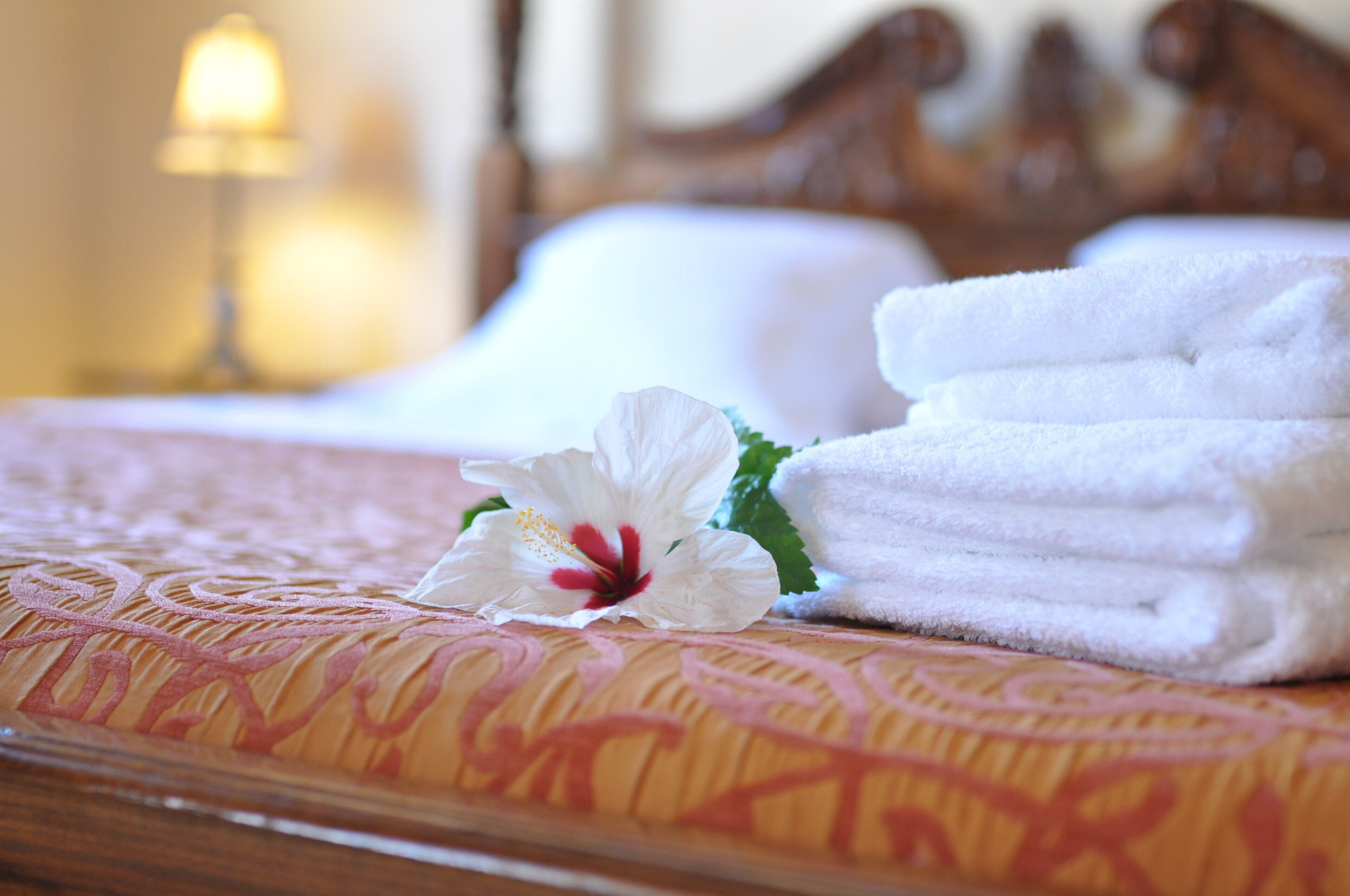 A neatly made bed with white towels and a hibiscus flower.