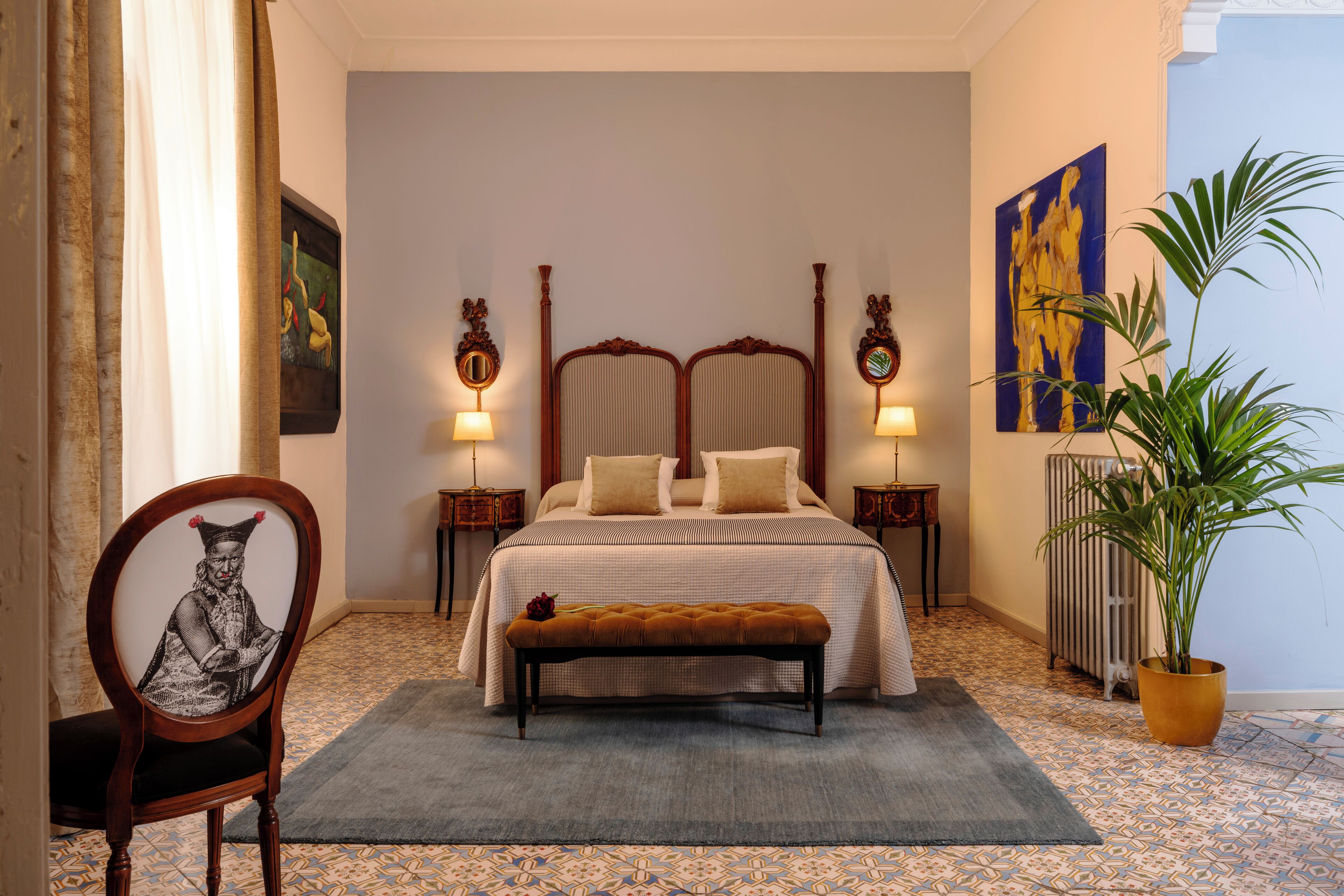 A bedroom with a bed, a bench, a chair, a radiator, and a potted plant.