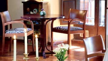 Comedor con una mesa dispuesta para cuatro, con platos blancos, cubiertos y un candelabro. Hay dos sillas con cojines a rayas azules y blancas, y un aparador de madera con adornos.