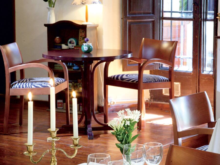Comedor con una mesa dispuesta para cuatro, con platos blancos, cubiertos y un candelabro. Hay dos sillas con cojines a rayas azules y blancas, y un aparador de madera con adornos.