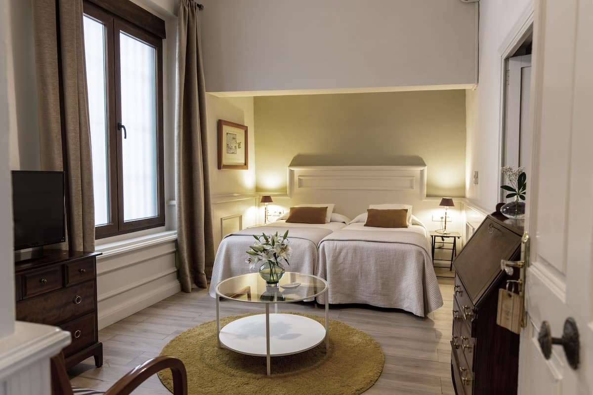 Habitació d'hotel amb dos llits, una televisió, una taula de vidre amb un ram i un calaixera de fusta.