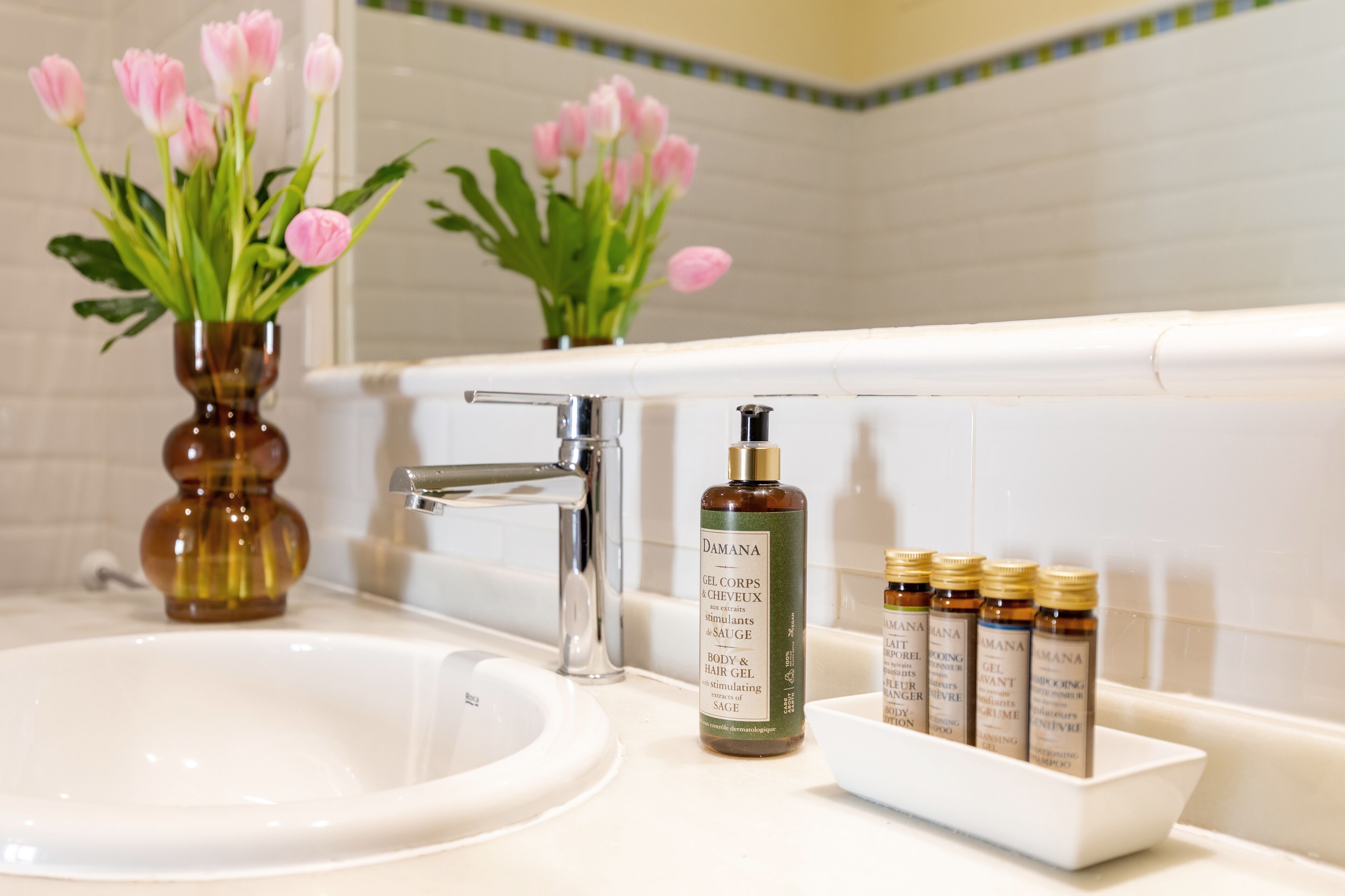 Een badkamer met een witte wastafel, een spiegel en een rij toiletartikelen, waaronder een fles body- en haargel.