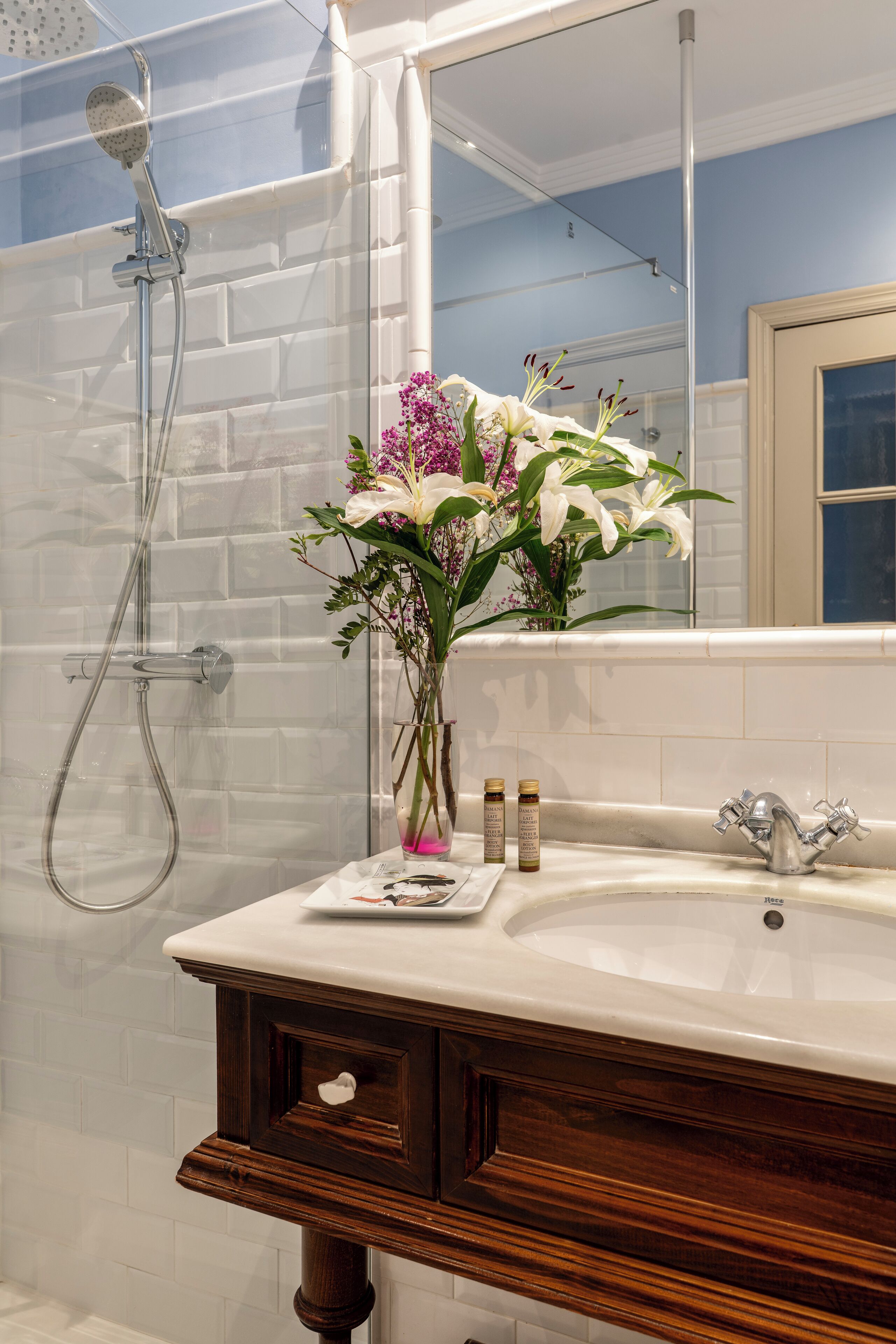 A bathroom with a shower, a sink with toiletries, and a mirror.