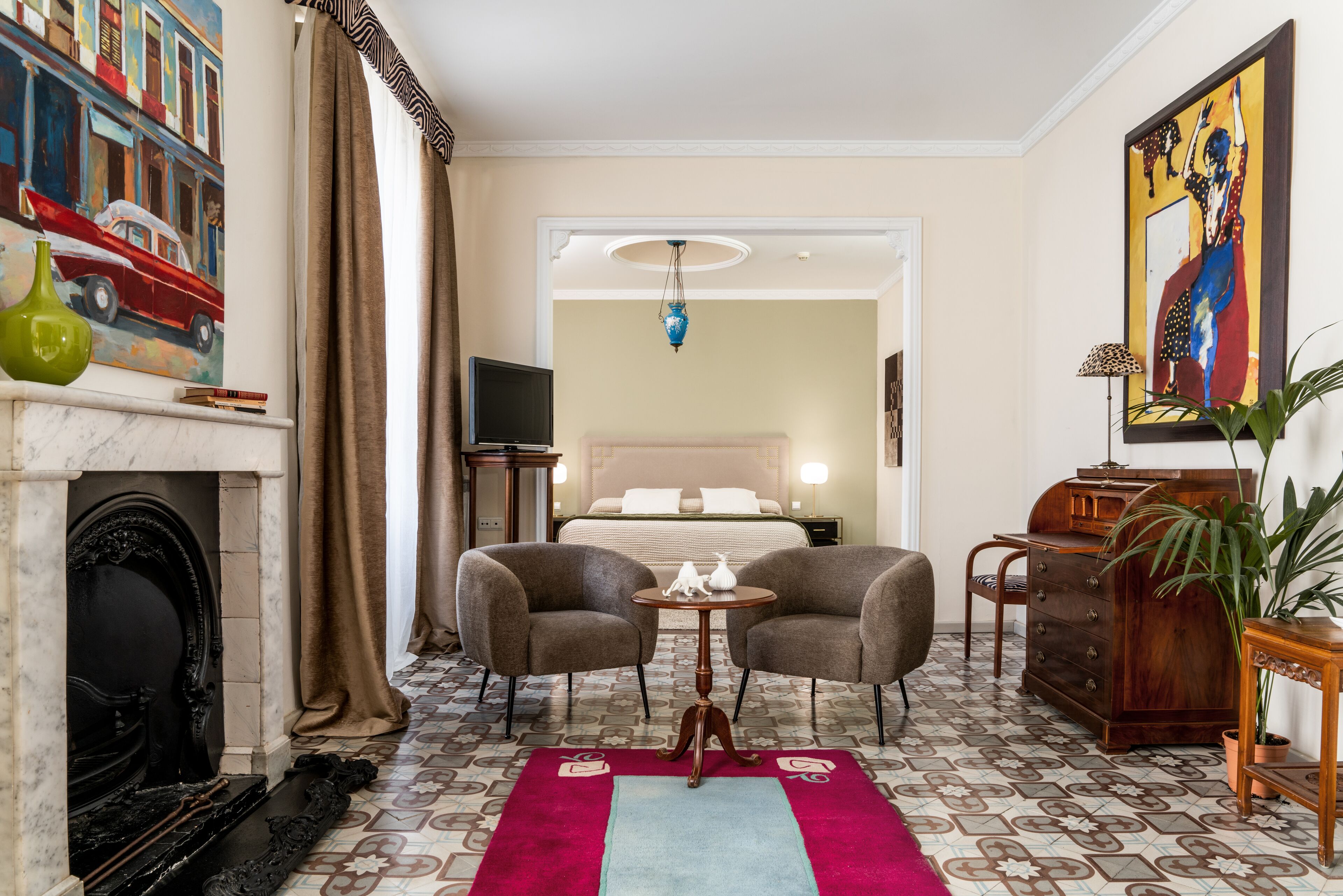 Ein Hotelzimmer mit Kamin, zwei Sesseln, einem kleinen Tisch, einem Bett mit Kopfteil, einem Fernseher und einem Gemälde an der Wand.