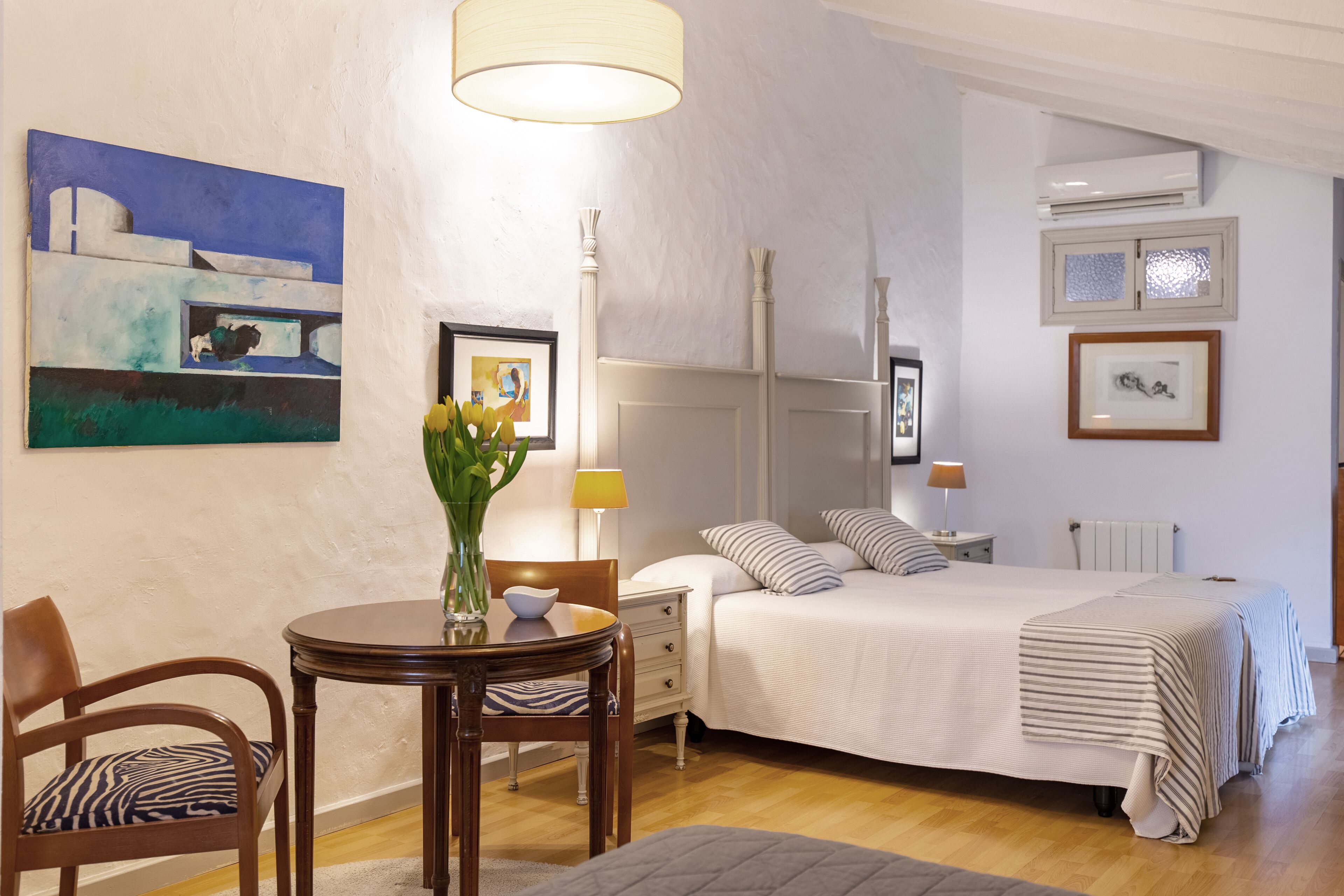 A bedroom with a bed, bedside table, lamp, and a painting on the wall.