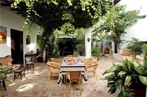 An outdoor patio with a table and chairs, surrounded by potted plants and a brick floor.