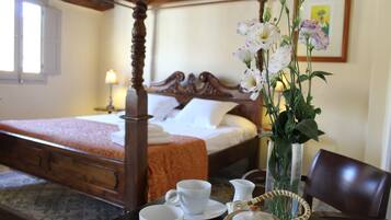 A hotel room with a four-poster bed, a vase with flowers, and a table with cups and a pitcher.