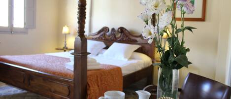 Une chambre d’hôtel avec un lit à baldaquin, un vase rempli de fleurs et une table avec des tasses et une carafe.