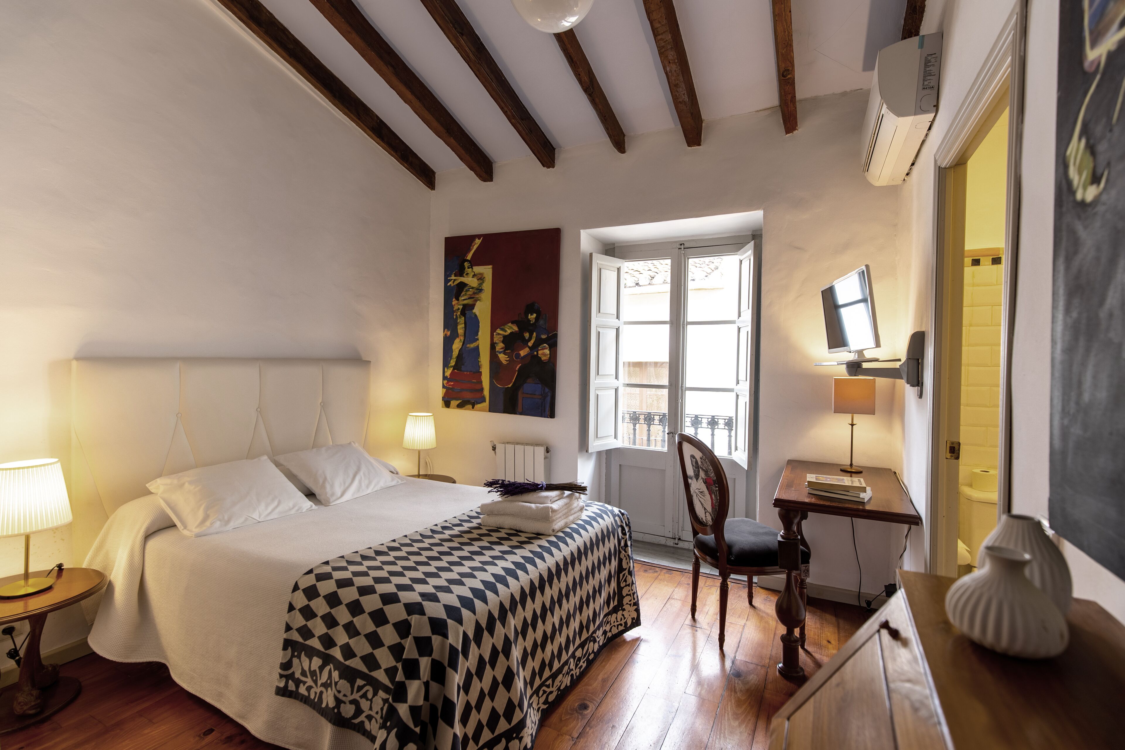 A bedroom with a bed, a desk, a chair, a window, and a painting on the wall.