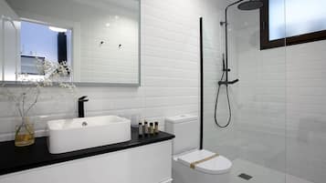 Un baño moderno con lavamanos blanco, encimera negra y cabina de ducha con mampara de vidrio.