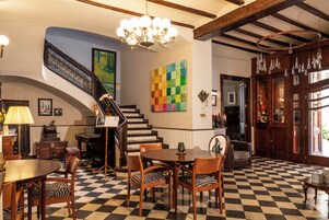 Un pavimento a scacchi, una scala, un'area pranzo con sedie, un lampadario e un'opera d'arte colorata al muro.