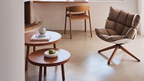 A modern interior with a large window offering a coastal view, a wooden table, a cushioned chair, and a fireplace. - Bill&Coo Mykonos (Mykonos)